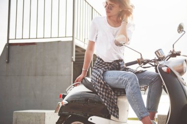 Güzel bir hippi kızın portresi siyah bir scooter 'da oturuyor, gülümsüyor poz veriyor ve ılık bahar güneşinin tadını çıkarıyor.