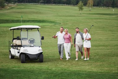 Genç çiftler oynamaya hazırlanıyor. Bir grup gülen arkadaş golf arabasıyla deliğe geldi..