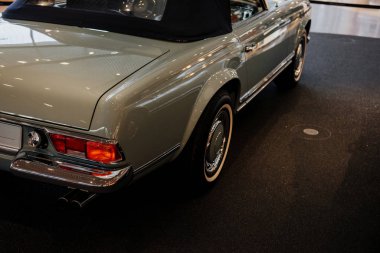 Sağ krom arka lambası ve egzoz borusuyla yakın gri arabanın gövdesinin ve tarafının üst kısmını, kahverengi zemindeki beyaz bir lastik üzerinde tekerlek kemerini,.