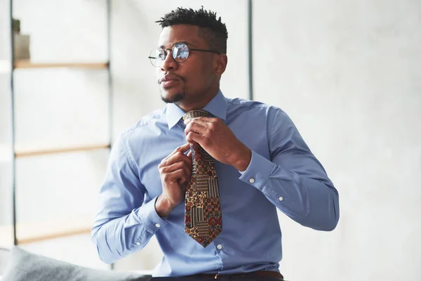 Fixing the tie. Photo of black stylish man getting wearing clothes and preparing for the work.