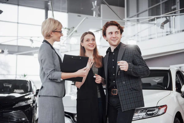 Buying their first car together. High angle view of young car salesman standing at the dealership telling about the features of the car to the customers.