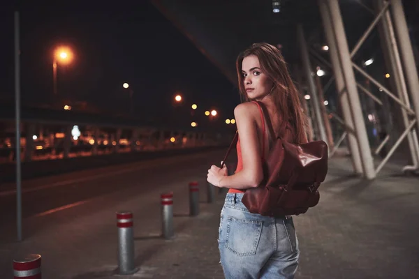 夏日温暖的夜晚 一个背着背包的年轻漂亮的姑娘站在机场或火车站附近的大街上 她刚到 正在等出租车或她的朋友 — 图库照片