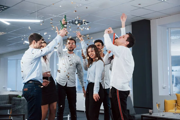 Everyone is happy. Photo of young team in classical clothes celebrating success while holding drinks in the modern good lighted office.