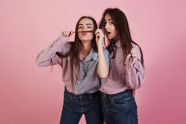 用头发做胡子在粉红背景的演播室里玩乐的年轻女人可爱的双胞胎 — 图库照片