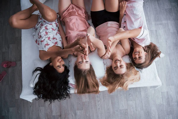 Give high five everyone. Inverted portrait of charming girls that lying on bed in nightwear. Top view.