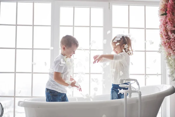 Child playing with rose petals in home bathroom. Little girl and boy fawing fun and joy together. The concept of childhood and the realization of dreams, fantasy, imagination.