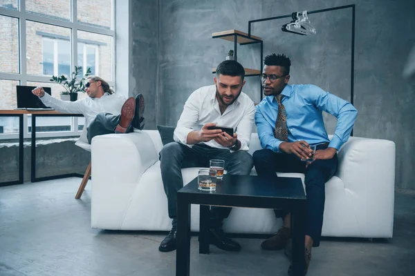 Feet on the couch. Relax time. Group of multiracial office workers in formal clothes talking about tasks and plans.