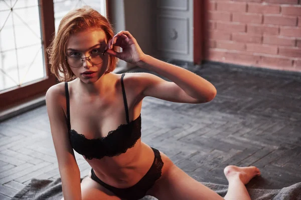 穿着眼镜和内裤的性感姑娘坐在靠近窗户的房间地板上 — 图库照片