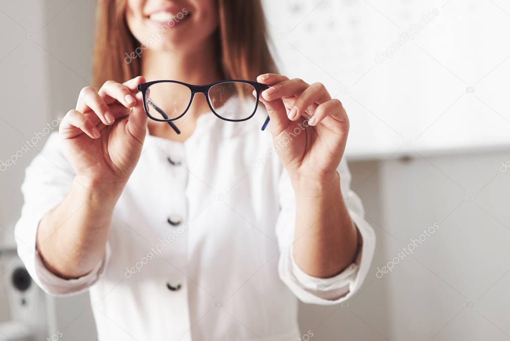 You can see the smile. Female doctor showing the eyeglasses by holding it in two hands.