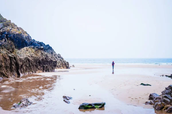 Mujer caminando en la playa de arena en la distancia en la bahía de Rhossili, Wa — Foto de Stock