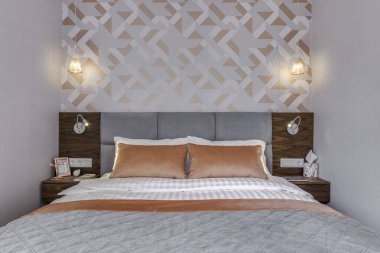 Budapest, Hungary - April 18, 2019: Luxurious bedroom with modern stylish rose gold wallpaper, coral pillows and wooden grey headboard.
