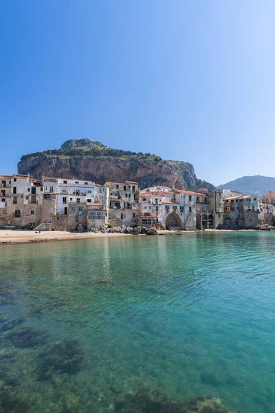 Idyllic view of turquoise sea and houses with Rocca di Cefalu rocky mountain in the background seen from historical old port of Cefalu - Sicily, Italy