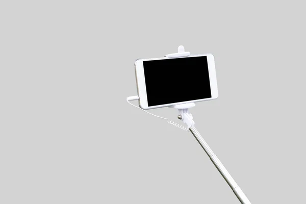 Egy selfie-bottal szürke háttér elszigetelt fehér smartphone. — Stock Fotó