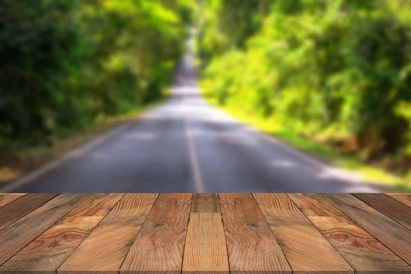 Brunt trä bord och suddiga vägen går genom skogen. — Stockfoto