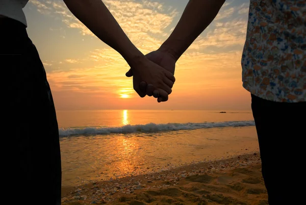 Pár tartja a kezét, és a gyönyörű naplemente a tengerparton — Stock Fotó
