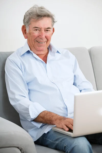Старший дорослий посміхається під час використання ноутбука — стокове фото