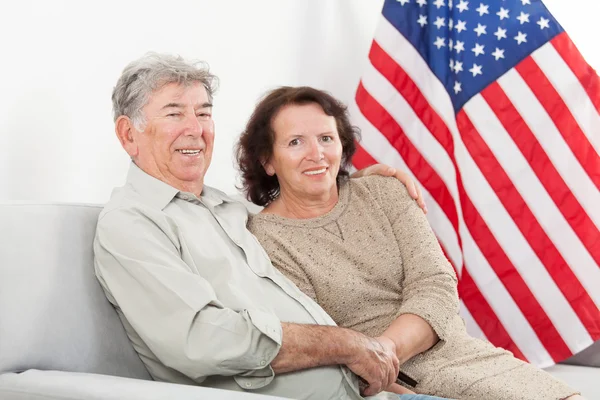 Casal sênior feliz sentado na frente da bandeira americana — Fotografia de Stock