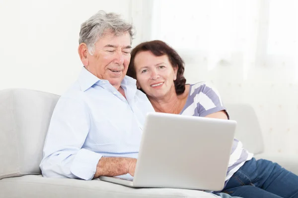 Старшая пара смеется во время использования ноутбука — стоковое фото