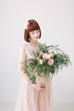 Çiçeklerle ayakta ve beline tutarak gülümseyen hamile kadın 