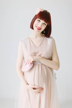 pembe elbiseli bebek için pembe ayakkabı tutan mutlu hamile kadın portresi