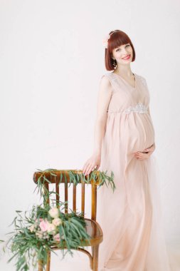 beyaz zemin üzerinde mumlar yanan ile dekore edilmiş sandalye yanında duran pembe elbiseli güzel hamile kadın