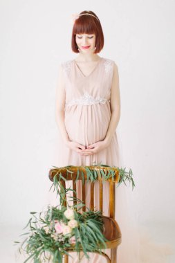 tam uzunlukta bir şekilde dekore edilmiş sandalyeye duran hamile kadın