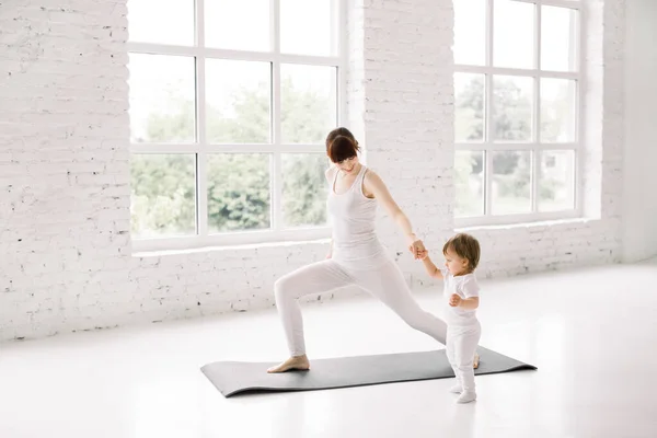 young mother does physical fitness exercises, lunges together with her little baby