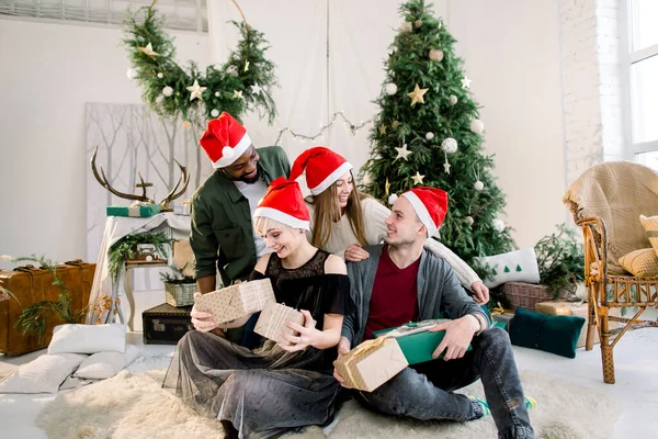 Fröhliche junge vier internationale Menschen feiern gemeinsam Weihnachten und Neujahr im gemütlich dekorierten Atelier. — Stockfoto