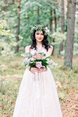 Kafasında okaliptüs çelengi olan genç ve güzel bir gelinin portresi, düğün yürüyüşünde ormanda kırsal bir buket ile..