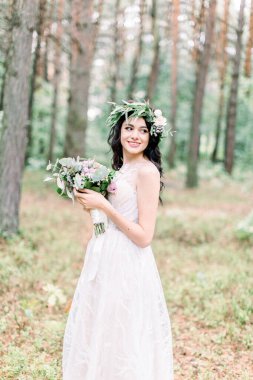 Yeşil orman boyunca harika mutlu gelinin yürüyüşü. Güzel, gülümseyen gelin esmer, beyaz elbiseli, düğün çiçekli genç kadın.