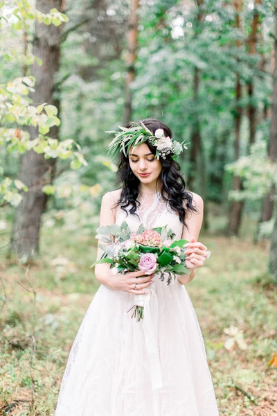 beautiful bride in nature in a coniferous forest in a wreath on her head and a luxurious wedding dress. Rustic boho style of wedding outdoors