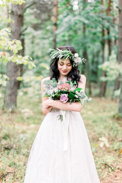Hermosa novia en la naturaleza en un bosque de coníferas en una corona en su cabeza y un vestido de novia de lujo. Estilo boho rústico de boda al aire libre —  Fotos de Stock
