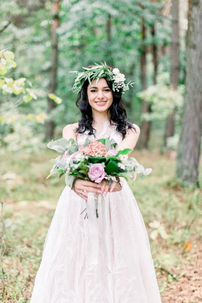 Portrait d'une jeune mariée avec une couronne d'eucalyptus sur la tête, avec un bouquet rustique dans la forêt lors d'une promenade de mariage . — Photo