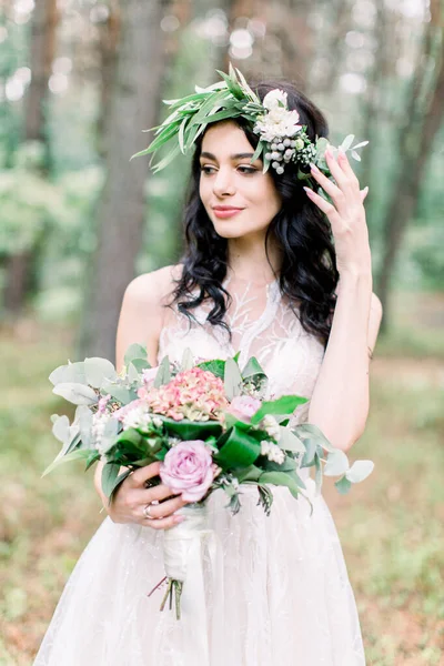 Retrato de una novia con un ramo de bodas en el bosque. Novia feliz en vestido elegante blanco, con un ramo de bodas, hermoso paisaje forestal en el fondo. Maquillaje natural, peinado, corona —  Fotos de Stock