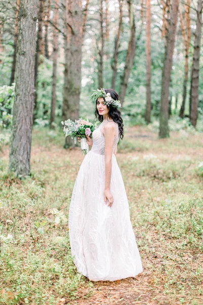 Belle mariée avec une couronne sur la tête et avec un bouquet à la main dans le style rustique est dans un parc ou une forêt, la marche et le sourire — Photo