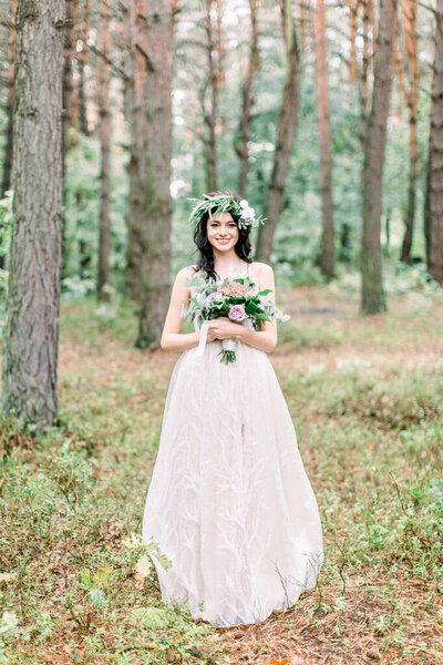 Stylish bride posing with bouquet on background of forest, luxury gorgeous boho wedding at forest outdoors.
