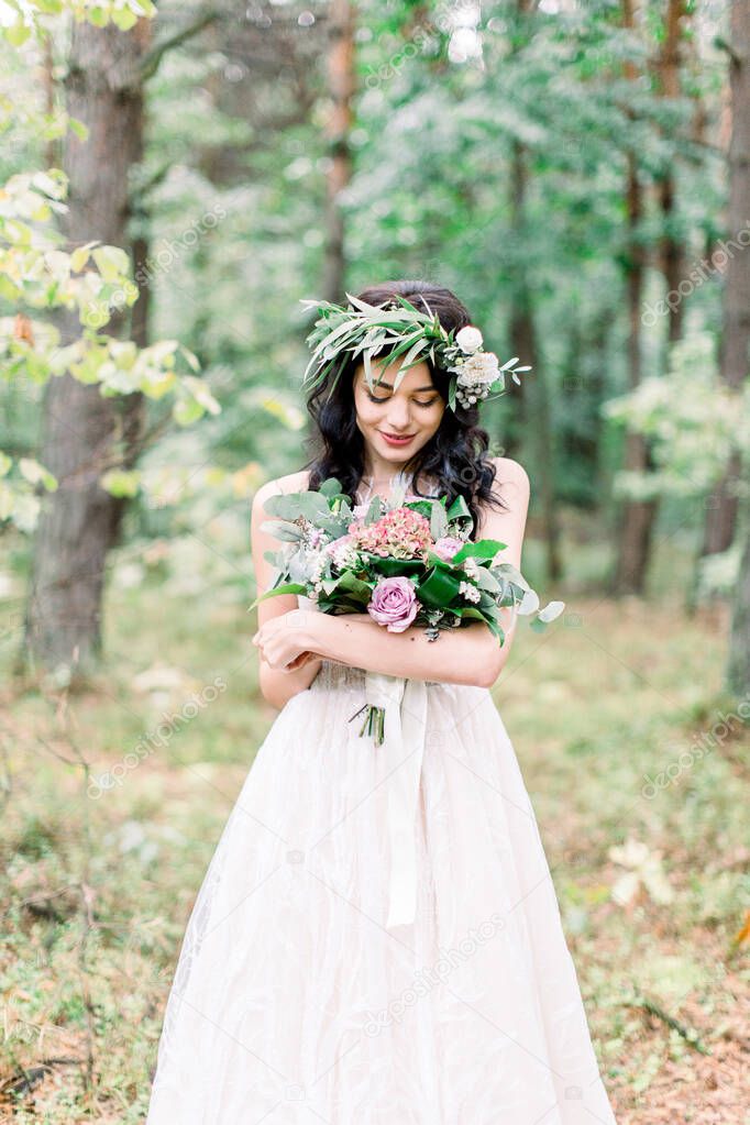 beautiful bride in nature in a coniferous forest in a wreath on her head and a luxurious wedding dress. Rustic boho style of wedding outdoors