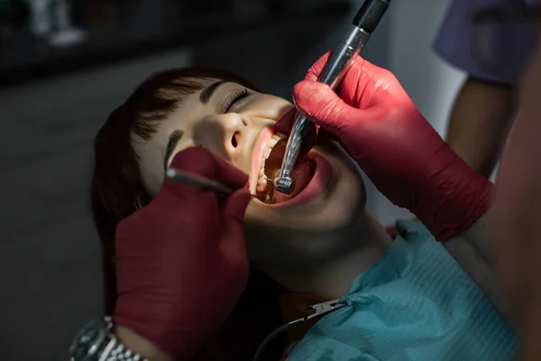 Dentista sênior do sexo masculino dente de perfuração para jovem paciente do sexo feminino em cadeira dentária — Fotografia de Stock