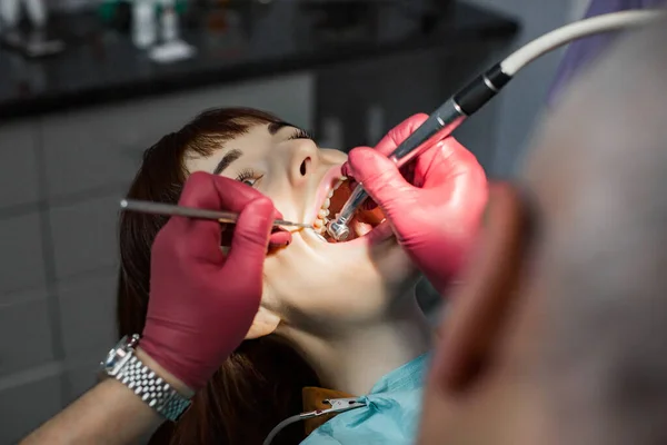 Senior male dentist drilling tooth to young female patient in dental chair