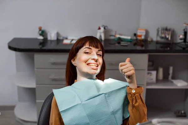 Feliz joven sonriente mujer mostrando el pulgar hacia arriba sentado en el consultorio del dentista después del examen dental y el tratamiento indoloro. copyspace, felicidad, servicio al paciente, salud, medicina dental —  Fotos de Stock