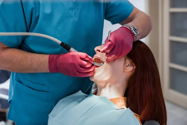 Lekarz dentysta w gabinecie stomatologicznym przeprowadzający operację zębów dla młodej kobiety w nowoczesnej klinice stomatologicznej — Zdjęcie stockowe