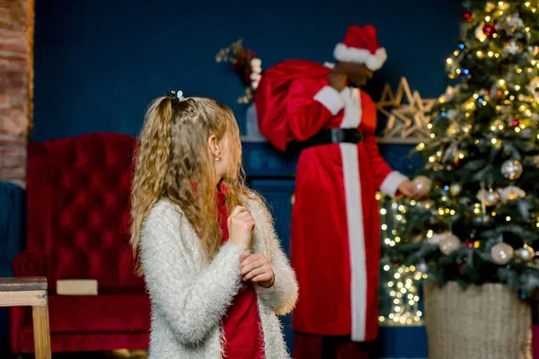 Niña está feliz de que Santa Claus vino y pone regalos en el árbol de Navidad — Foto de Stock