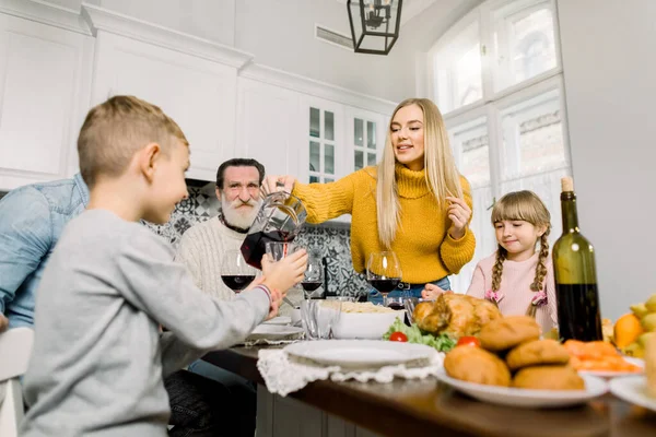 Hezká mladá matka nalévá synovi třešňovou šťávu na sváteční večeři. šťastná velká rodina s prázdninovou večeří v den Díkůvzdání — Stock fotografie