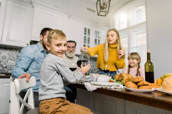 Festliches Abendessen in glücklicher Familie. Seitenansicht eines kleinen Jungen, der ein Glas mit Saft hält. glückliche Familienmitglieder, Großvater, Mutter, Vater und Schwester schauen und lächeln — Stockfoto