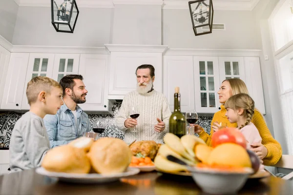 Mehrgenerationenfamilie feiert Erntedank. alter Opa mit grauem Bart hält Glas mit Rotwein und spricht die Wünsche aus und stößt an — Stockfoto