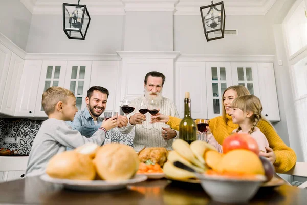 Bonne grande famille assise à une table à la maison pour le dîner de Thanksgiving faire un toast avec des verres de vin rouge. Grand-père, parents et deux enfants — Photo