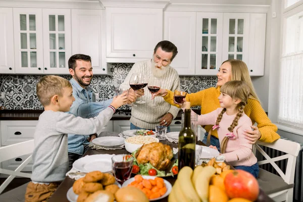 Beautiful family, grandfather, parents and children, clinking glasses of wine and juice on holiday dinner. Family at the table in cozy dining room at home — Stock Photo, Image