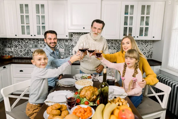 Seitenansicht einer glücklichen Mehrgenerationenfamilie, die zu Hause an einem gedeckten Tisch sitzt und mit einem Glas Rotwein anstößt. Großvater, Eltern und Kinder — Stockfoto