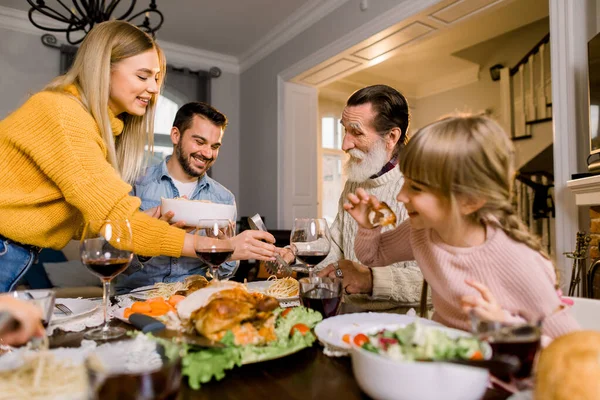 快乐的微笑着的家人、祖父、父母和孩子们坐在节日的餐桌前，享用着美味的晚餐。 妈妈把意大利面放在盘子里给家人吃 — 图库照片