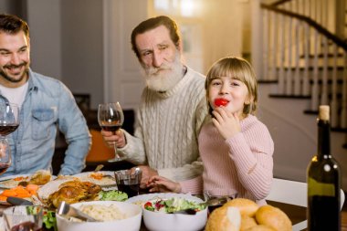 Çoklu Nesil Ailesi masada oturuyor ve lezzetli bir akşam yemeği yiyor, Şükran Günü 'nü kutluyor. Büyükbaba, yakışıklı baba ve küçük kız domates yiyor ve gülümsüyor.